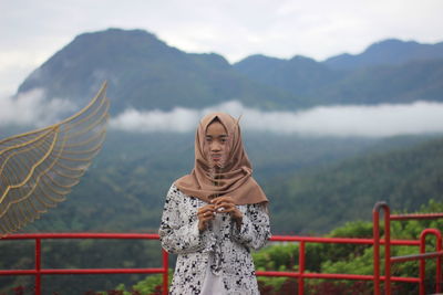 Portrait of woman wearing hijab holding crop against mountains