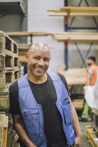 Happy bald carpenter leaning on wooden rack at warehouse