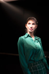 Portrait of young woman standing against black background