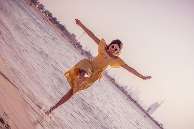 Woman with arms outstretched splashing water while standing at beach