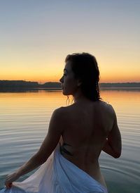 Woman standing at beach against sky during sunset