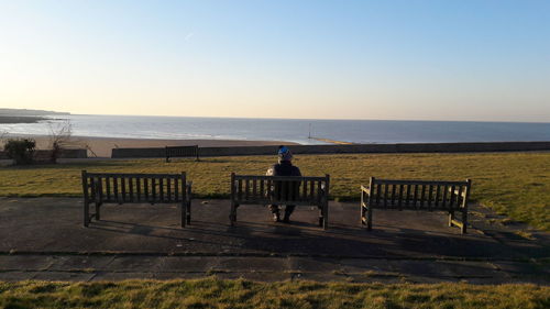 Rear view of man sitting by sea against clear sky