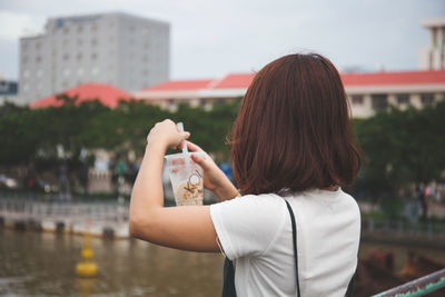 Rear view of woman photographing against city buildings