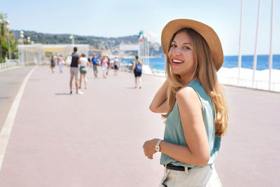 Portrait of attractive woman smiling at camera walking along promenade des anglais, nice, france