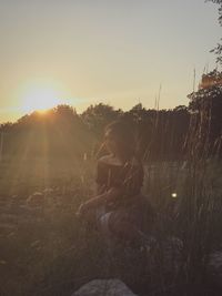 Boy sitting on field against clear sky during sunset