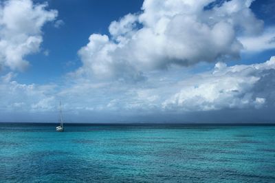 Boats in calm sea against cloudy sky