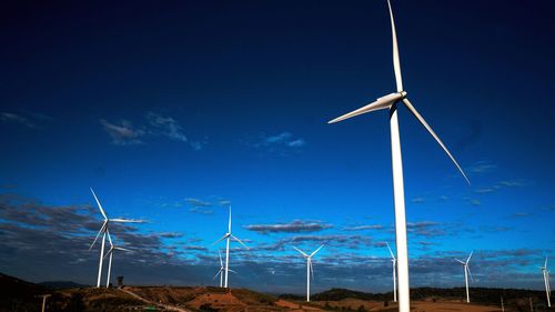 Low angle view of windmills on landscape against blue sky