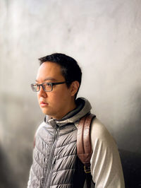 Portrait of young man wearing eyeglasses standing against wall