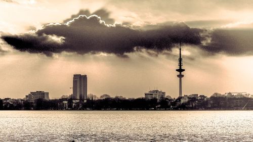 City at waterfront against cloudy sky