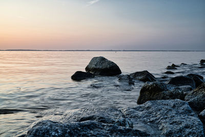 Rocks in sea against sky during sunset