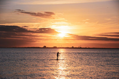 Silhouette man on sea against sky during sunset