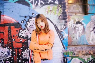 Portrait of young woman standing against graffiti