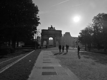 Silhouette people walking at city gate against sky during sunny day