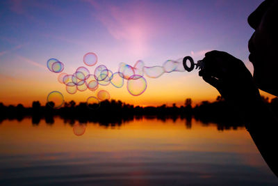 Close-up of person blowing bubbles by lake at sunset