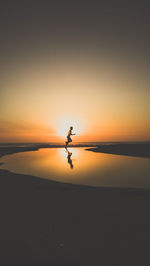 Silhouette man on beach against sky during sunset