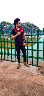 Young man looking away while standing against railing