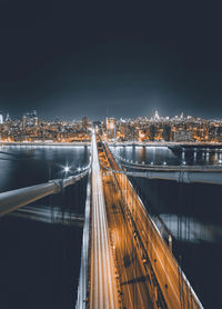 Illuminated manhattan bridge in city against sky at night