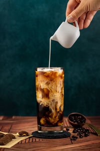 Midsection of person pouring drink in glass on table