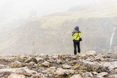 Rear view of man standing on cliff against mountains