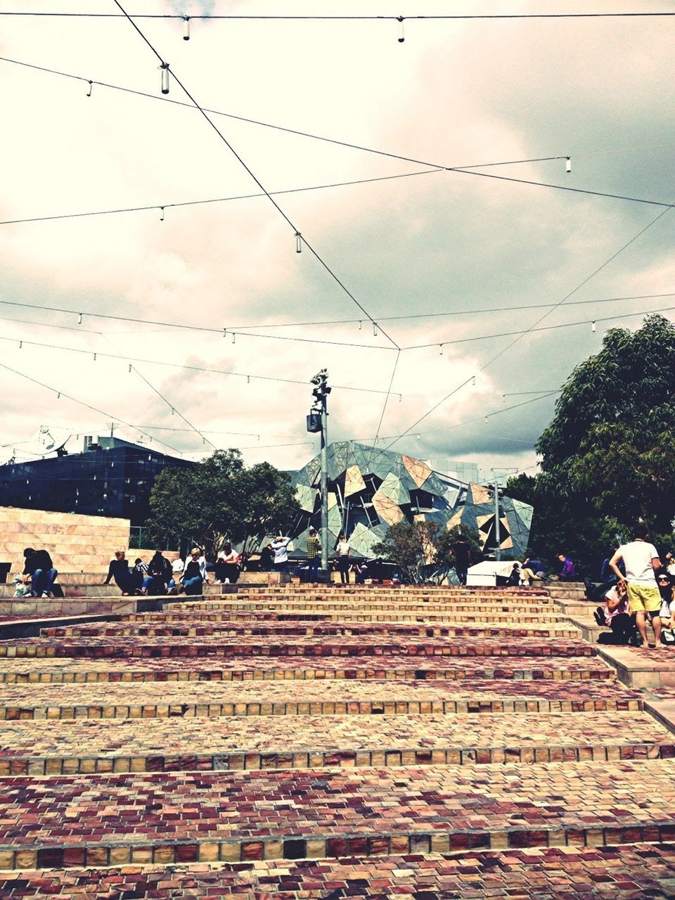 sky, men, large group of people, cloud - sky, lifestyles, person, transportation, leisure activity, power line, cable, bicycle, built structure, street, cloud, architecture, building exterior, medium group of people, land vehicle, walking