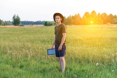 Young man farmer in cowboy hat at agricultural field on sunset holding tablet. happy man on nature 