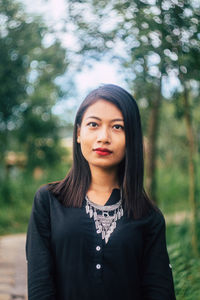 Portrait of young woman standing against trees