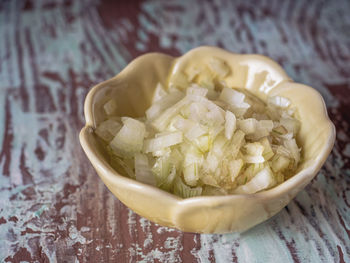 Finely chopped onions, preparation for salad in a pale yellow bowl on a brown table
