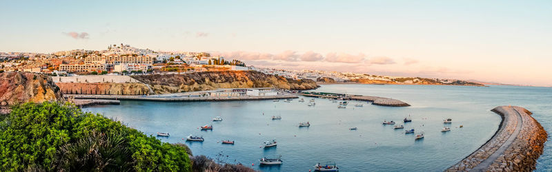 Panoramic view of boats moored on sea by city against sky