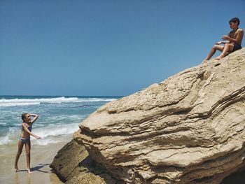 Woman on rock by sea against clear sky