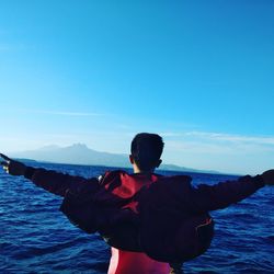 Rear view of man standing in sea against blue sky