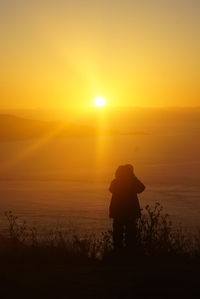 Rear view of silhouette man standing on field against sunset sky
