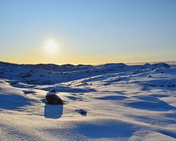 Snow covered landscape against sky during sunset