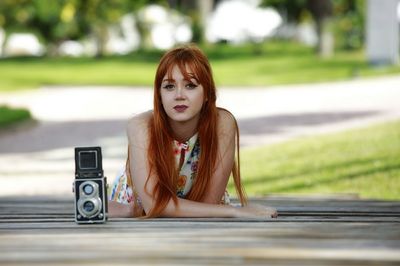 Portrait of beautiful redhead woman lying with vintage camera on footpath