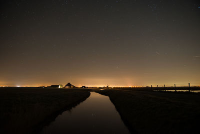 River amidst silhouette field against sky at dusk