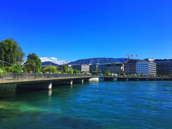 Bridge over river in city against clear blue sky