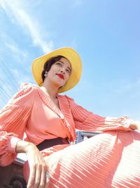 Low angle portrait of woman sitting against sky