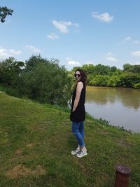 Full length of young woman standing by tree against sky