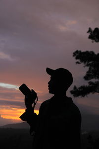 Silhouette man photographing against sky during sunset