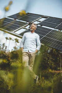 Thoughtful man with hands in pockets standing by solar panels