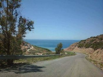 Road by sea against clear blue sky