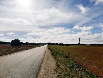 Empty road amidst field against sky