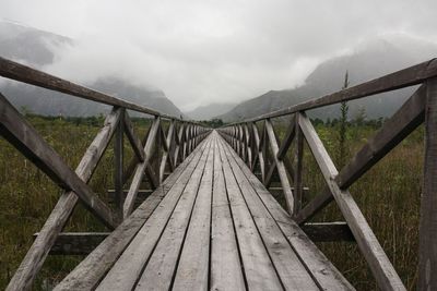 Footbridge by mountains against sky