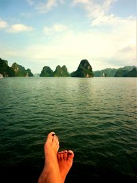 Low section of man relaxing by sea against sky