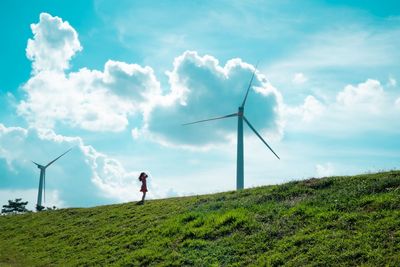 Rear view of woman walking on field against sky, beside windmill