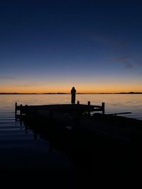 Silhouette man on pier by sea against sky during sunset