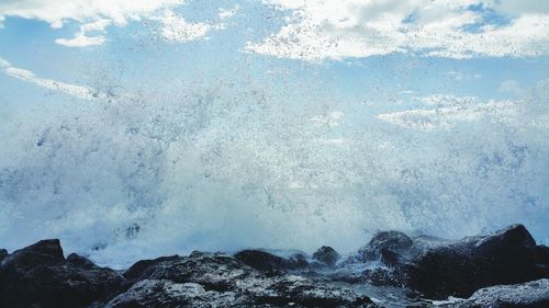 Water splashing on rocks against sky