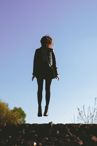 Low angle view of woman levitating against clear sky