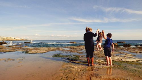 Family playing at beach against sky on sunny day