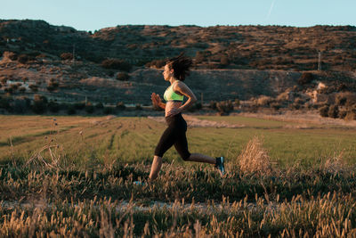 Full length of woman running on field against sky