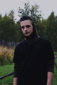 Portrait of young man standing against trees on field